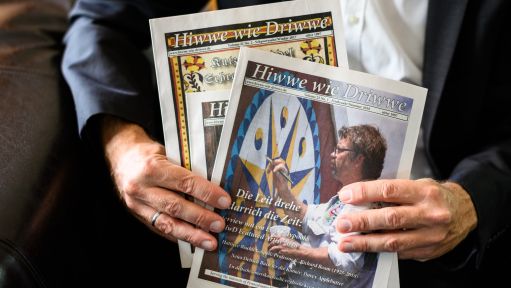 Michael Werner, Herausgeber, hält mehrer Zeitschriften „Hiwwe wie driwwe“ in seinen Händen. In Ober-Olm wird eine Zeitschrift „Hiwwe wie driwwe“ (Hüben wie drüben) herausgegeben, die in dem pfälzischen Dialekt Pennsylvania-Deutsch geschrieben wird. Sie wird in den USA und hier gelesen. 