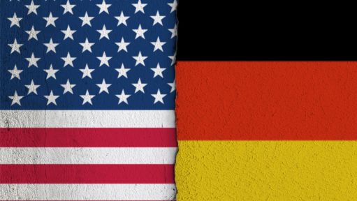 Die Nationalflaggen der Vereinigten Staaten von Amerika und der Bundesrepublik Deutschland auf einer Wand mit einem vertikalen Absatz bzw. Riss in der Mitte und zwei unterschiedlichen Putzarten. Foto mit Composing als Symbolbild für das Verhältnis zwischen den USA und der BRD.
