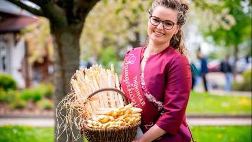 Die Thüringer Spargelkönigin 2024, Magdalena Schieck, hält lächelnd einen Korb frischem Spargel. 