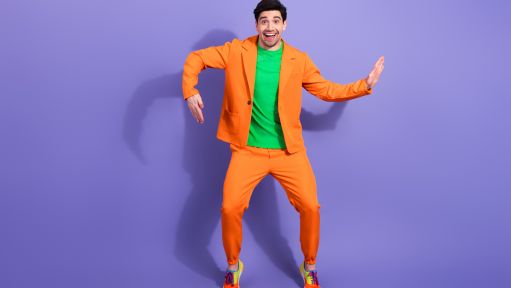 Mann in orangefarbenem Anzug vor lilafarbener Wand