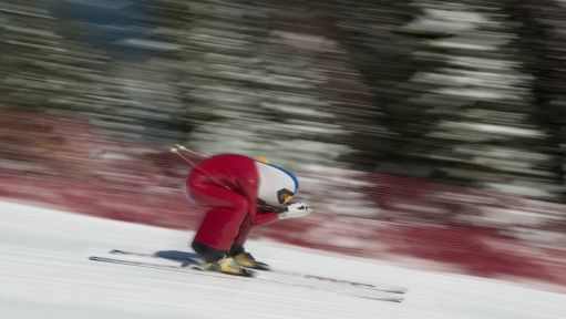 Ein Speed-Skifahrer im roten Anzug fährt die Piste herunter.
