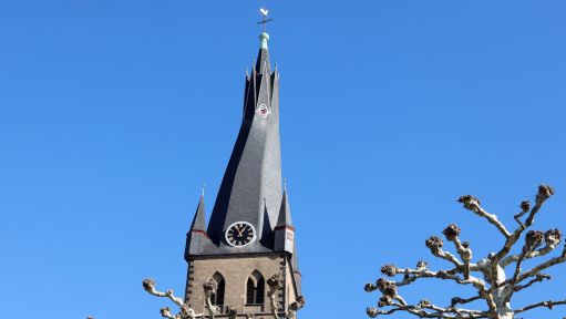 Vor einem Kirchturm stehen Bäume. 