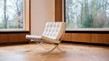 路德维希·密斯·凡德罗和莉莉·瑞希于 1929 年设计的巴塞罗那椅，摆放在一个铺着镶木地板、配有大窗户的房间里。