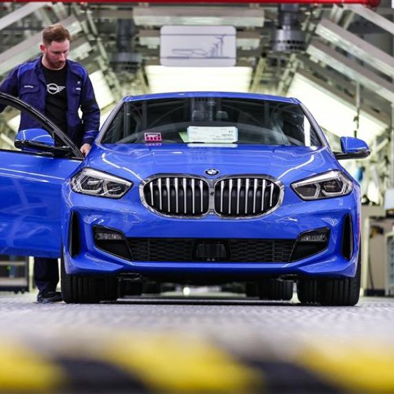 Ein Firmenmitarbeiter stehet neben einem blauen BMW 1er, der im BMW Group Werk Leipzig vom Band läuft.