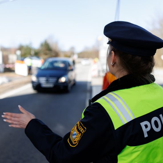 Eine Polizistin der Bayerischen Grenzpolizei stoppt ein Fahrzeug mit einem Handzeichen.