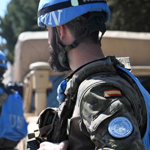 Ein Soldat ist von hinten zu sehen. Er trägt eine blaue Weste mit der Aufschrift UN und hat einen blauen Überzug über seinem Helm.