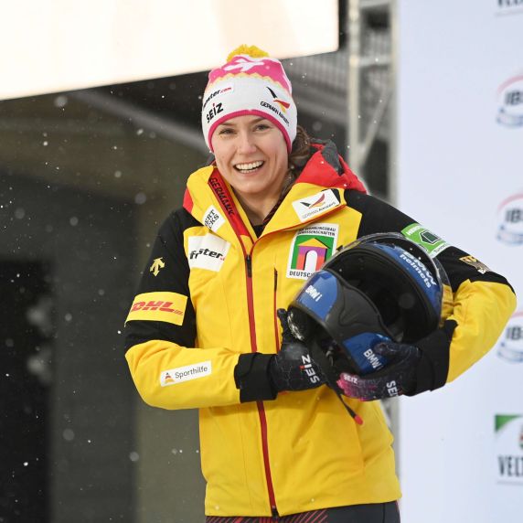 Portrait der deutschen Bobfahrerin Laura Nolte. Sie trägt die offizielle Kleidung des deutschen Wintersportteams und hält ihren Bob-Helm unter dem Arm.