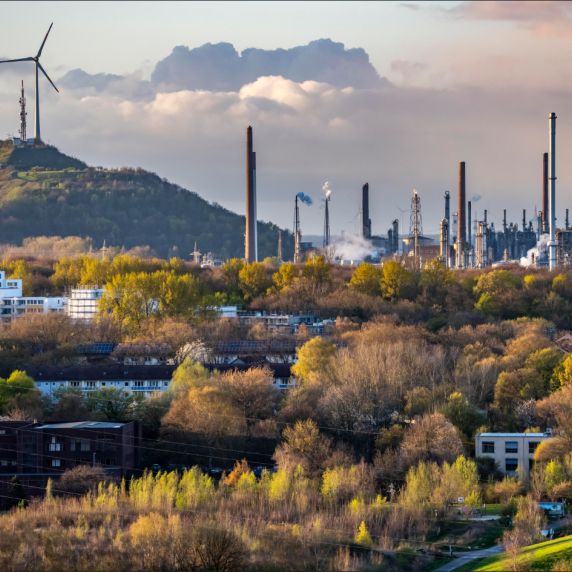 Industrielandschaft mit Raffinerieanlagen, hohen Schornsteinen und aufsteigendem Dampf 