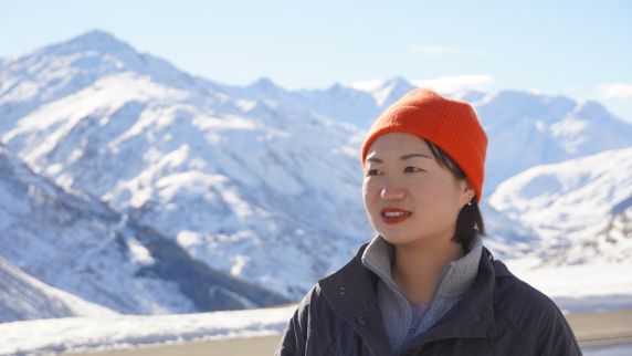 Junge Chinesin vor hohen schneebedeckten Bergen