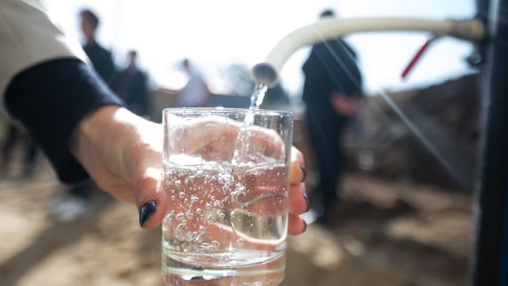 Wasser fließt aus einem Hahn in ein Glas.
