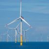 Mehrere Offshore-Windräder stehen im Meer vor blauem Himmel, mit einer großen Turbine im Vordergrund. 