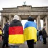 Eine Person mit einer Deutschland- und eine Person mit einer Ukraine-Flagge um die Schulter stehen vor dem Brandenburger Tor in Berlin