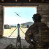 Soldat in Tarnuniform sitzt in einem Gebäude und steuert eine Drohne, die durch eine Maueröffnung ins Freie fliegt.
