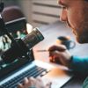 Ein Mann mit Kopfhöhrern sitzt vor einem Labtop und einem Mikrofon 