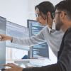 Frau und Mann in Büro vor mehreren Computerbildschirmen 