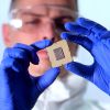 Ein Mann in Schutzanzug und mit Handschuhen hält einen Chip in der Hand.