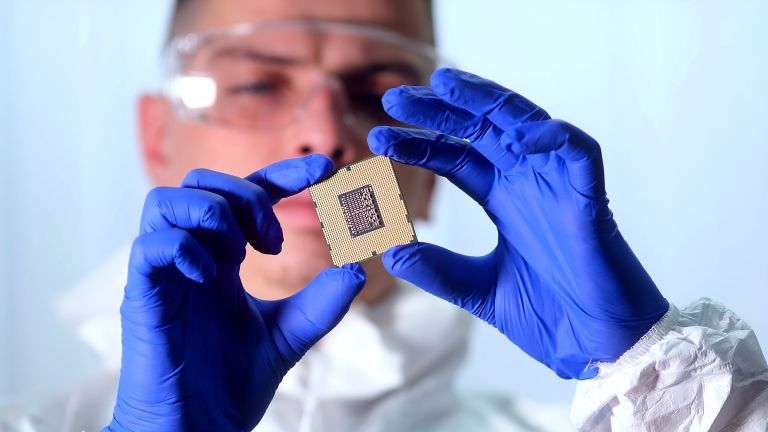 Ein Mann in Schutzanzug und mit Handschuhen hält einen Chip in der Hand.
